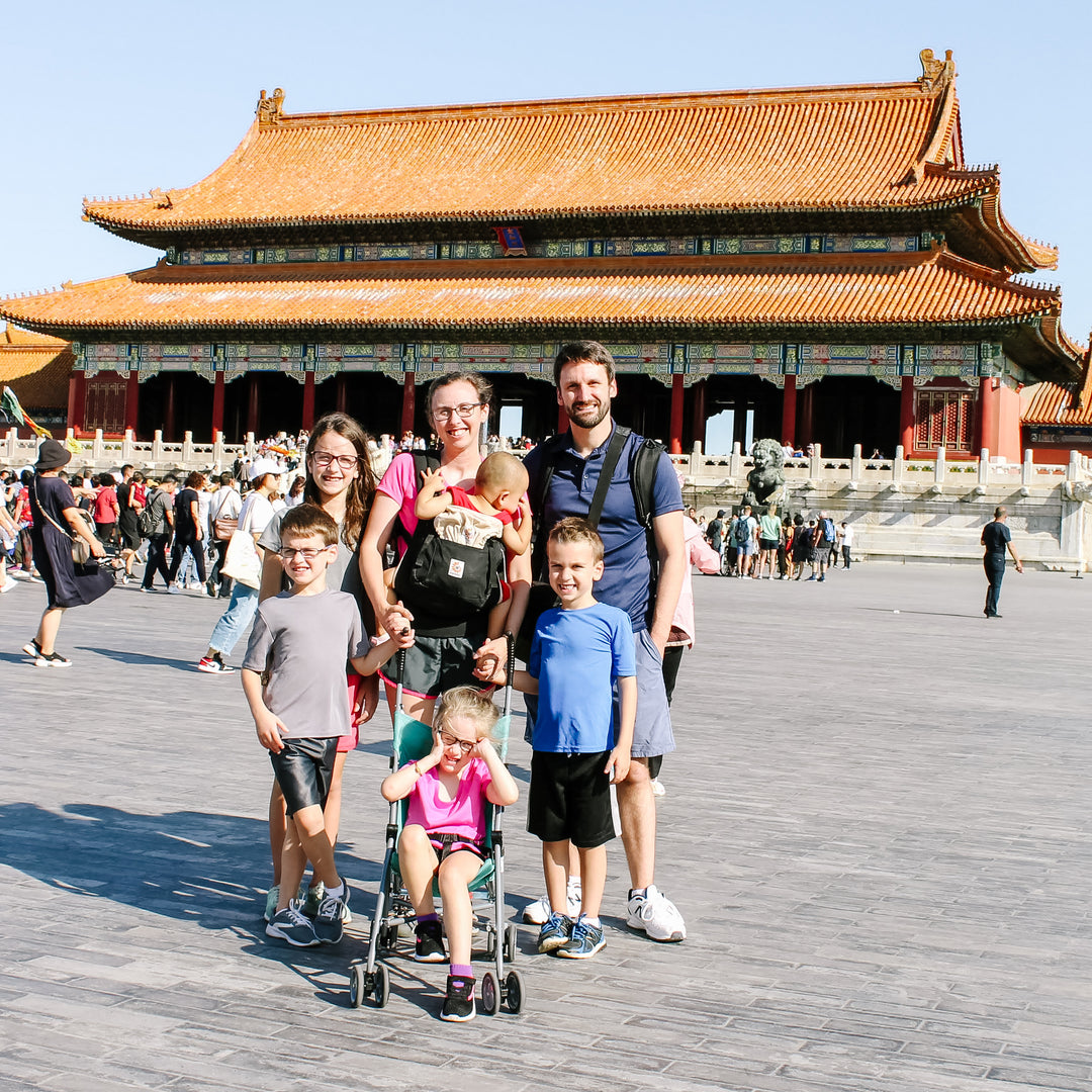 The author Jessica Deen Norris, her husband, and her five children smile for a photo. They are in China with the Forbidden City in the background.