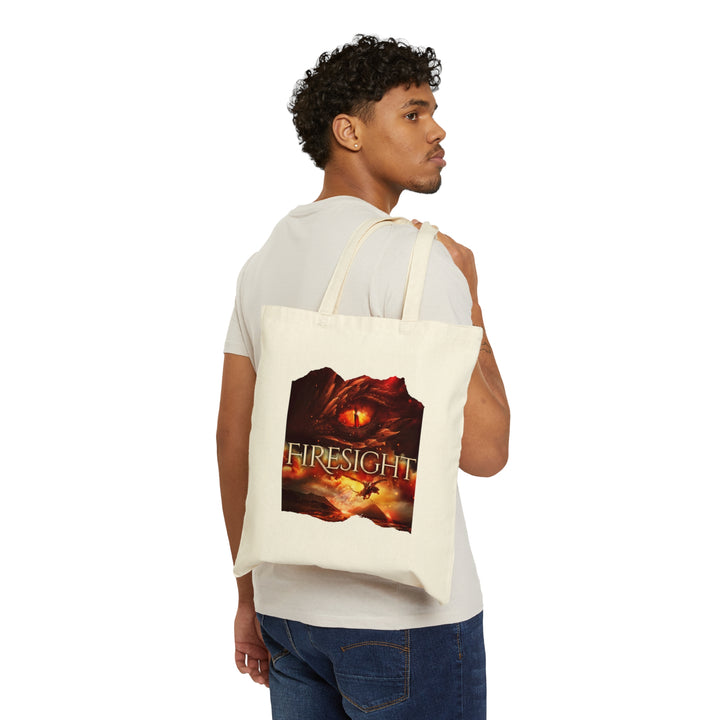 Someone holding a tan canvas tote bag. Design on the tote bag is the cover of Firesight, just showing the red dragon eye and the title with the two main characters riding on a dragon over a volcano erupting.