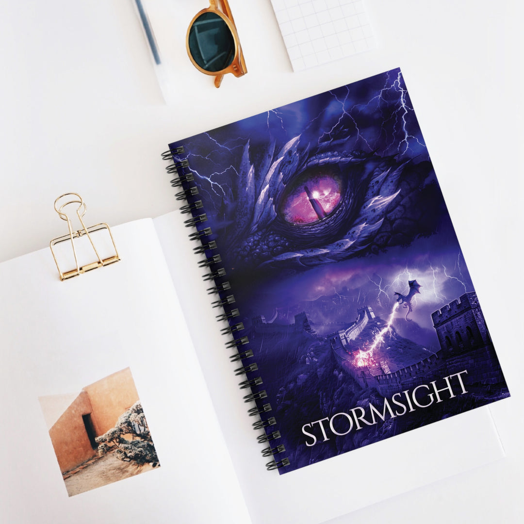 A notebook with the cover featuring the artwork from the cover of Stormsight. Artwork features a purple dragon eye at the top. Below the eye, a dragon breathes lightning onto a wall. The title is at the bottom of the notebook cover.