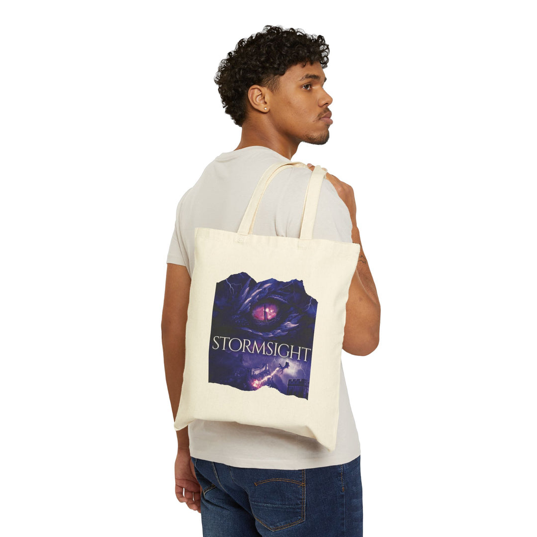 A person holding a tote bag. Design on the bag is the cover of Stormsight, just showing the purple dragon eye and the title with the a dragon breathing lightning onto a wall.