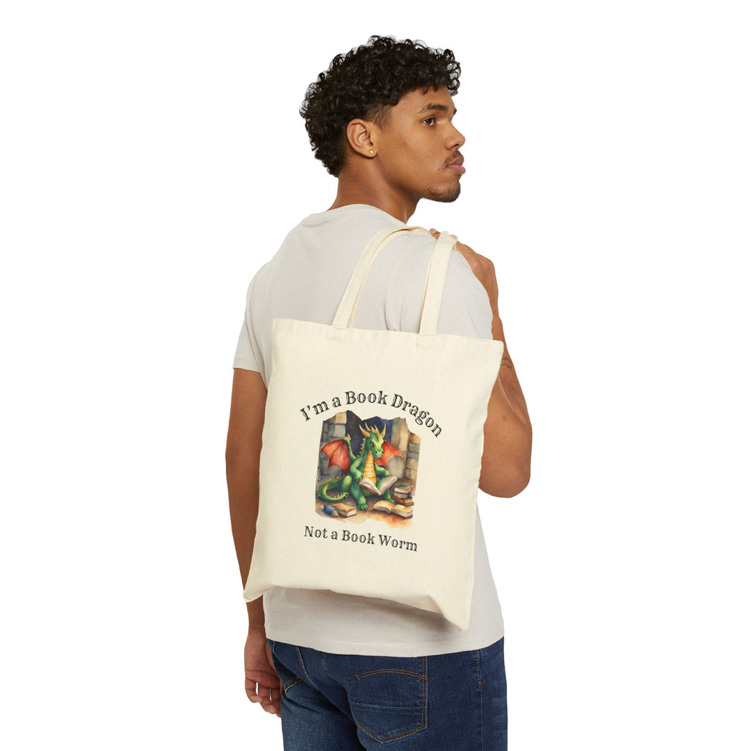 Someone holding a canvas tote bag. Design on the bag reads "I'm a book dragon not a book worm." Between the text is a watercolor design of a dragon reading next to a stack of books.