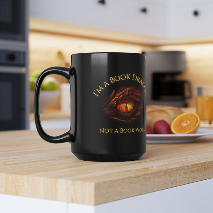 A black mug sitting on a table. Design on the mug reads "I'm a book dragon not a book worm." Between the text is the red dragon eye from the cover of Firesight.