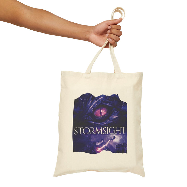 A person holding a tote bag. Design on the bag is the cover of Stormsight, just showing the purple dragon eye and the title with the a dragon breathing lightning onto a wall.