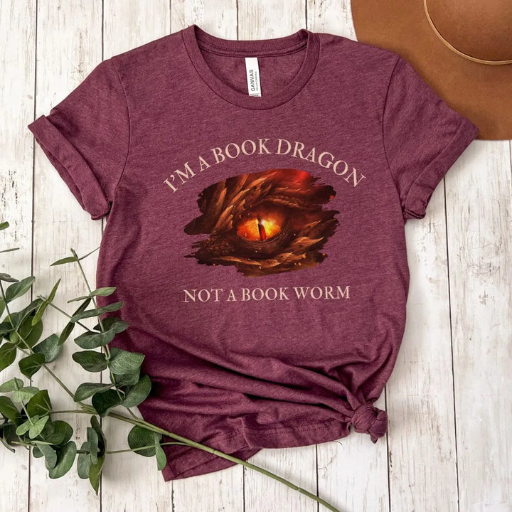 A short sleeve heather maroon t-shirt. Design on the shirt reads "I'm a book dragon not a book worm." Between the text is the red dragon eye from the cover of Firesight.