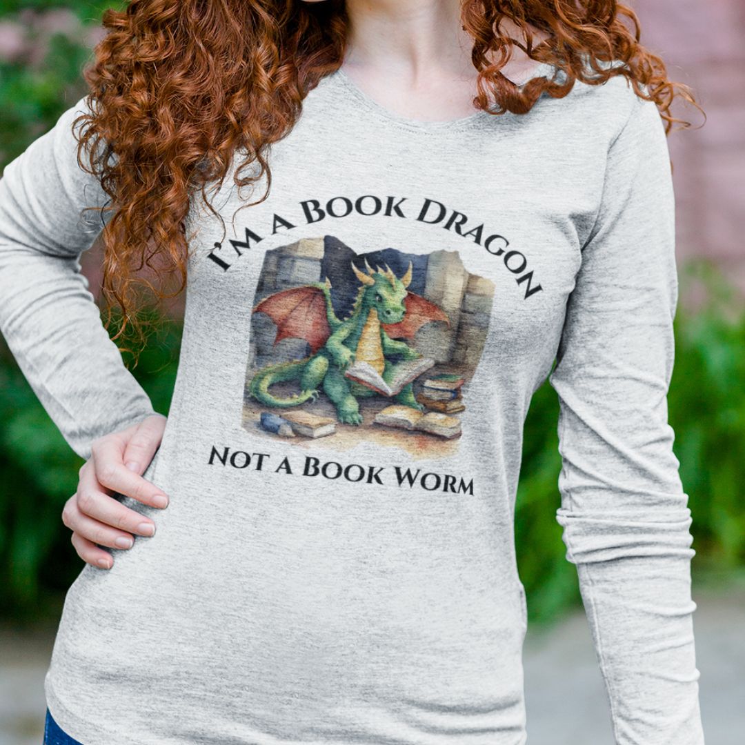 A woman wearing a long sleeve heather gray t-shirt. Design on the shirt reads "I'm a book dragon not a book worm." Between the text is a watercolor design of a dragon reading next to a stack of books.