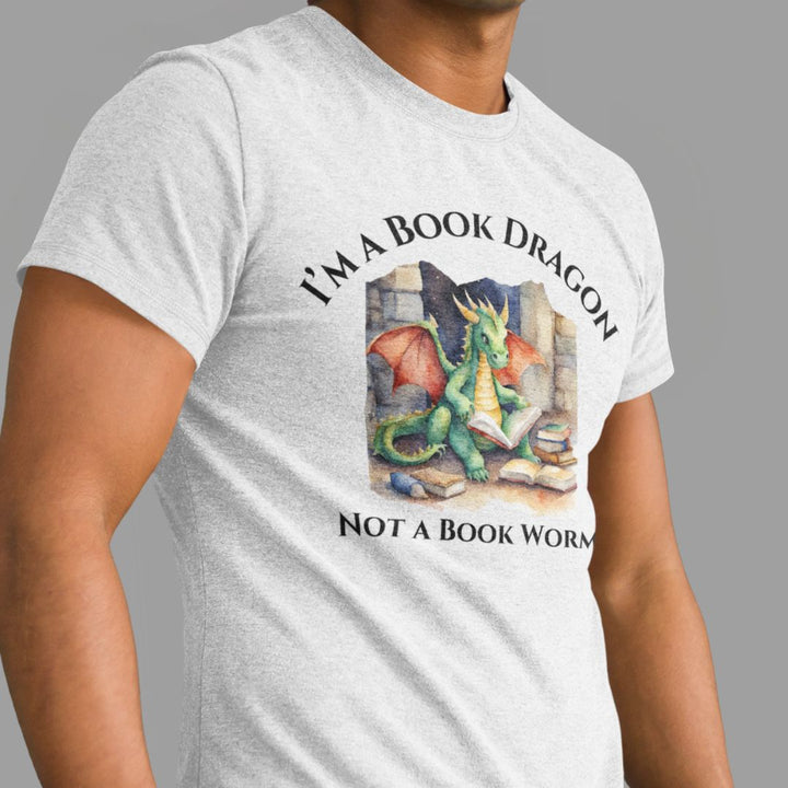 A man wearing a short sleeve heather gray t-shirt. Design on the shirt reads "I'm a book dragon not a book worm." Between the text is a watercolor design of a dragon reading next to a stack of books.