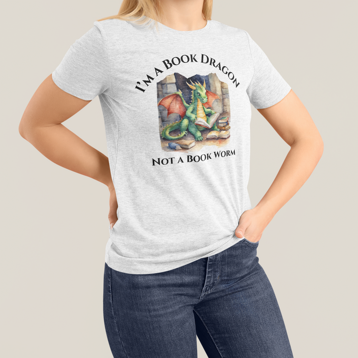 A woman wearing a short sleeve heather gray t-shirt. Design on the shirt reads "I'm a book dragon not a book worm." Between the text is a watercolor design of a dragon reading next to a stack of books.