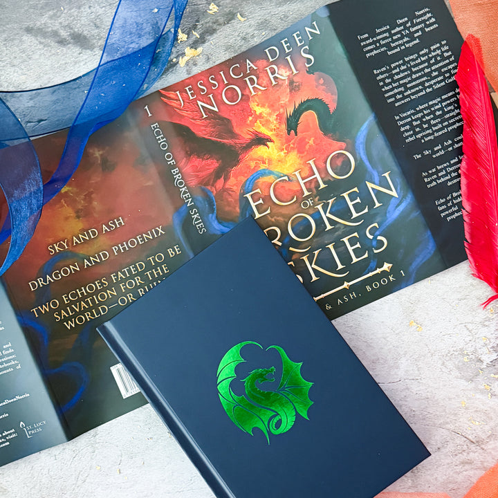 Hardcover - Echo of Broken Skies by Jessica Deen Norris - Dust jacket features a sky divided by swirling clouds of fire. On the left, a red phoenix with outstretched wings flies toward a dark green dragon on the right, both poised as if mid-battle. Blue, smoky tendrils swirl around the bottom of the image. Sprayed edges feature the dragon and phoenix. Cover is navy blue with a foiled green dragon silhouette centered on the book.#autograph-option_unsigned