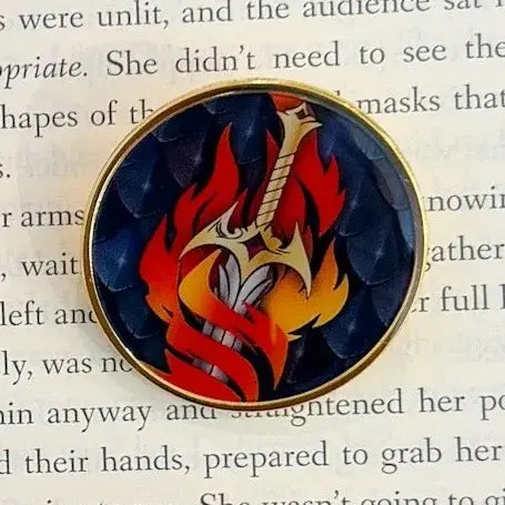 Circular pin with a sword and flames on a book page