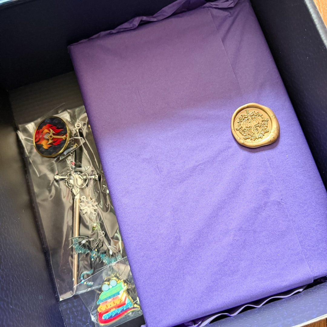 Omnibus wrapped in purple tissue with a gold dragon wax seal, plus sword bookmark and enamel pins inside the box
