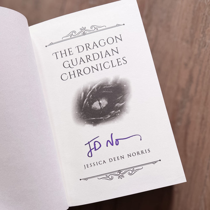 Signed book titled 'The Dragon Guardian Chronicles' by Jessica Deen Norris on a wooden surface