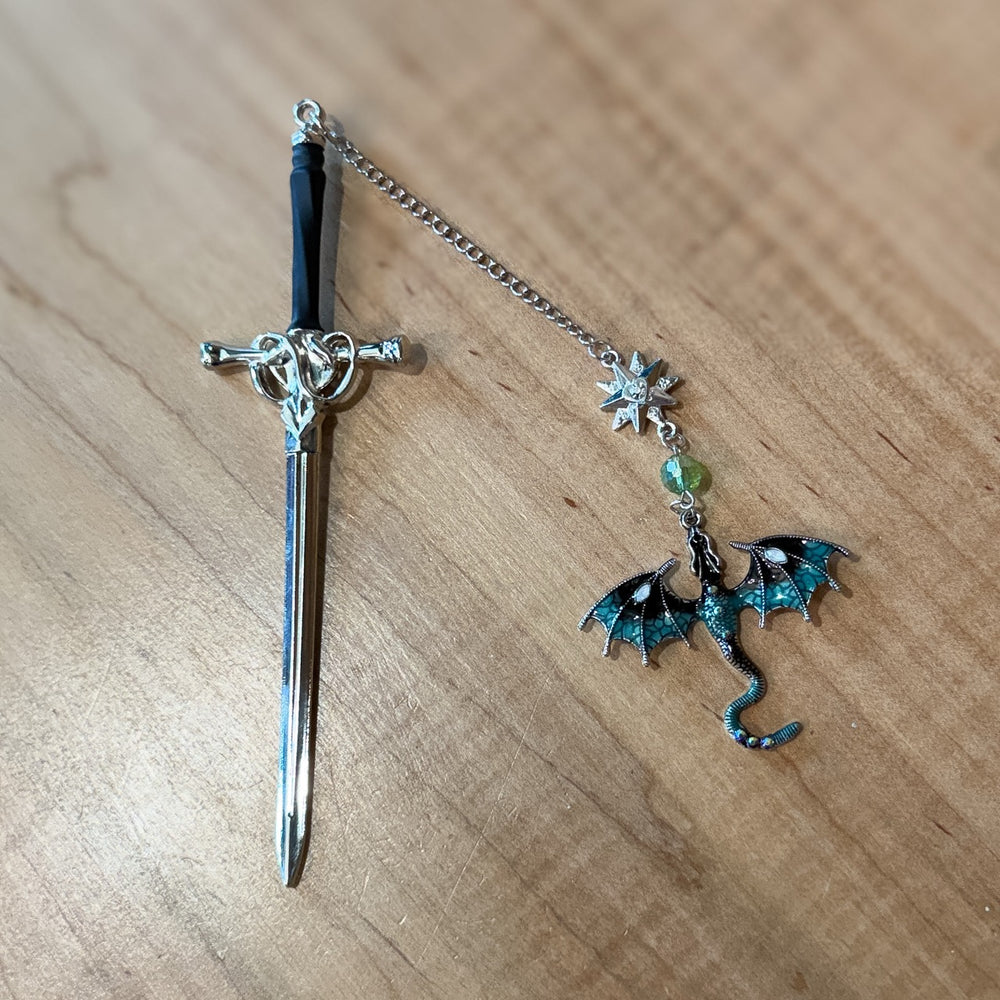 Decorative sword bookmark with a dragon charm on a wooden surface