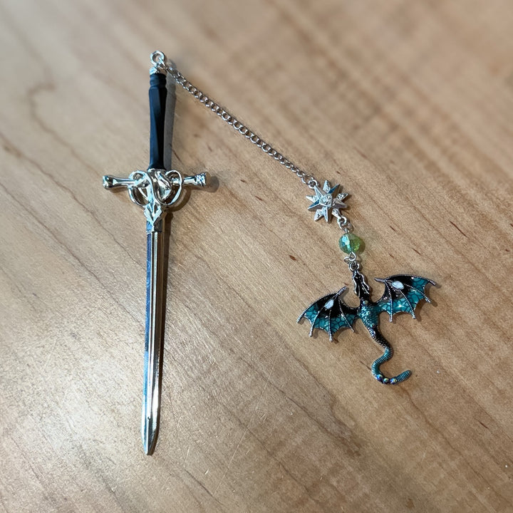 Decorative sword bookmark with a dragon charm on a wooden surface