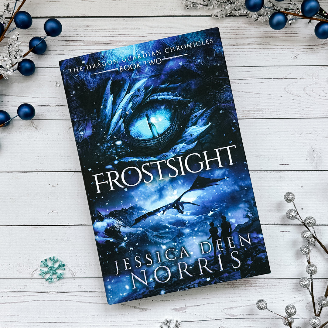 Frostsight hardcover cover. Cover features the title across the middle with a blue dragon eye and "The Dragon Guardian Chronicles Book 2" above it. Below the title, the two main characters watch a dragon in the distance in a snowy mountain landscape. The author's name is at the bottom of the cover.