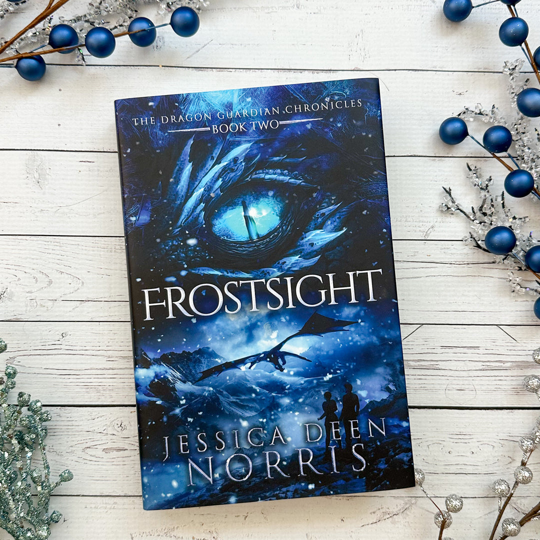 Frostsight hardcover cover. Cover features the title across the middle with a blue dragon eye and "The Dragon Guardian Chronicles Book 2" above it. Below the title, the two main characters watch a dragon in the distance in a snowy mountain landscape. The author's name is at the bottom of the cover.#autograph-option_unsigned