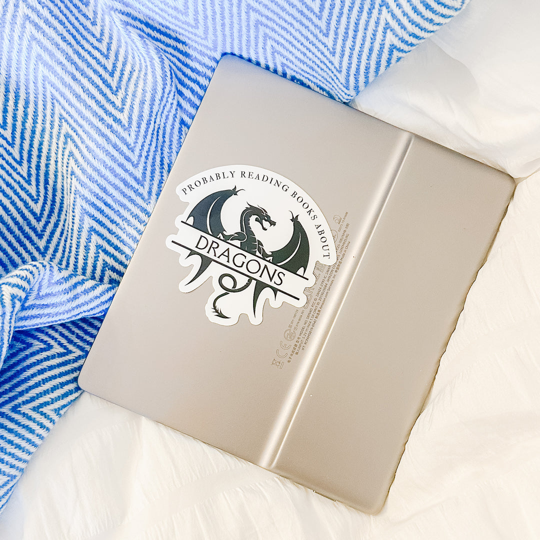 A white vinyl sticker on a Kindle with a black design that reads "Probably reading books about dragons." The word "dragons" is set apart on top of a large dragon.