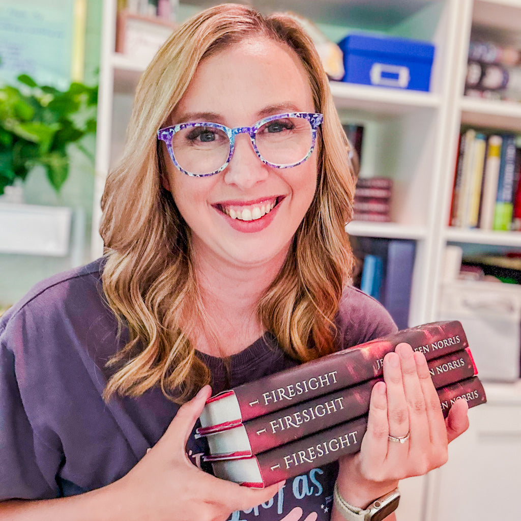 The author Jessica Deen Norris smiling and holding a stack of copies of her first book, Firesight