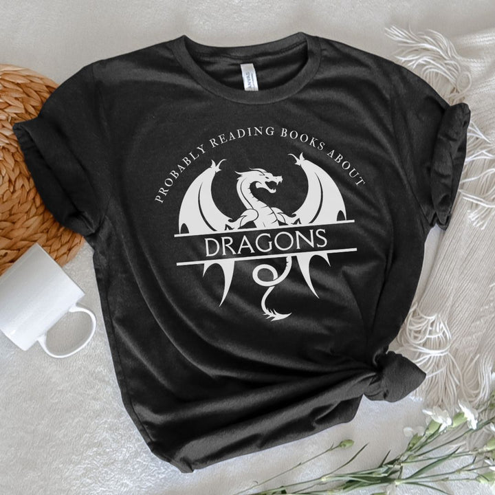 A short sleeve heather black t-shirt. The white design on the shirt reads "Probably reading books about dragons." The word "dragons" is set apart on top of a large dragon.