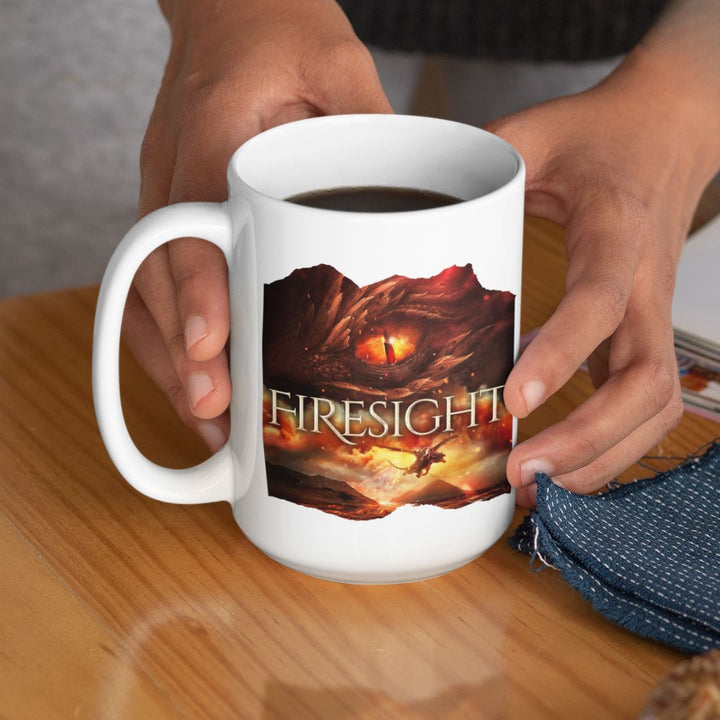 Someone holding a white mug. Design on the mug is the cover of Firesight, just showing the red dragon eye and the title with the two main characters riding on a dragon over a volcano erupting.